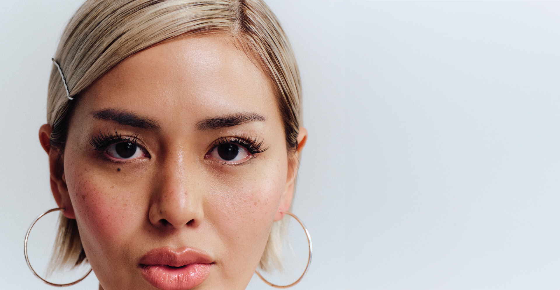 Close-up of a person with blonde hair and hoop earrings against a light background